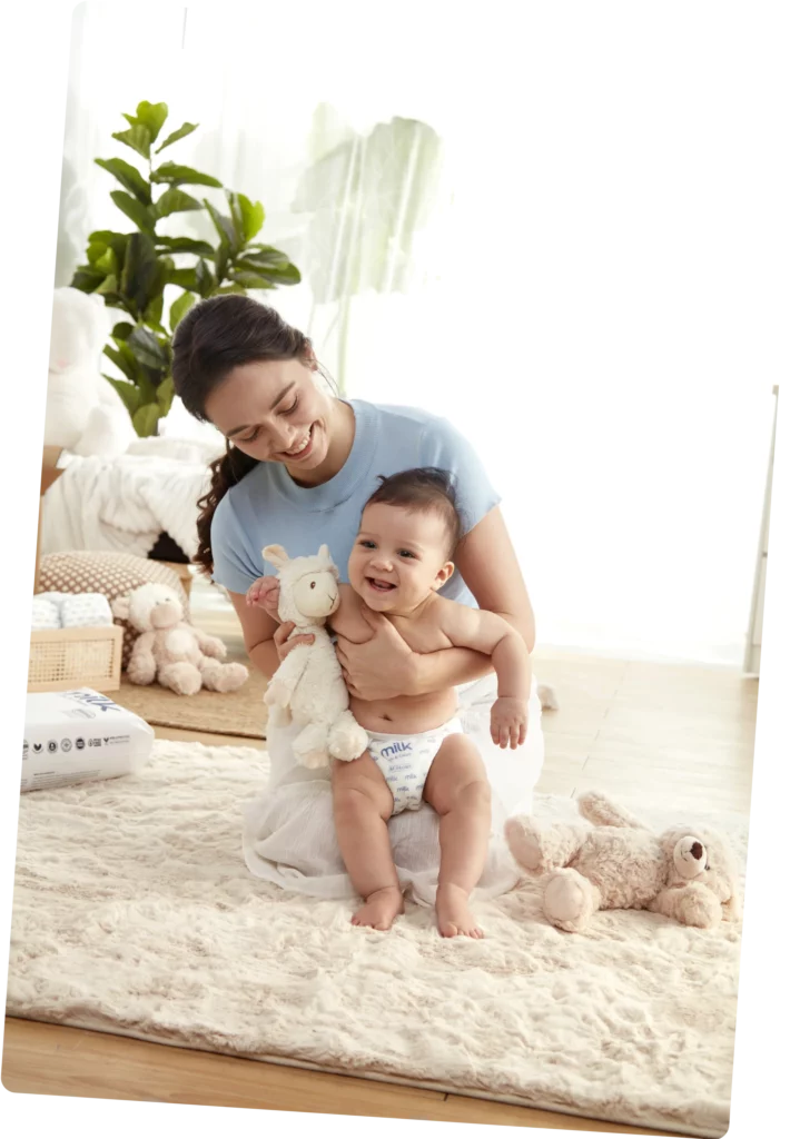 Mother carrying baby wearing MILKâ„¢ Diapers.